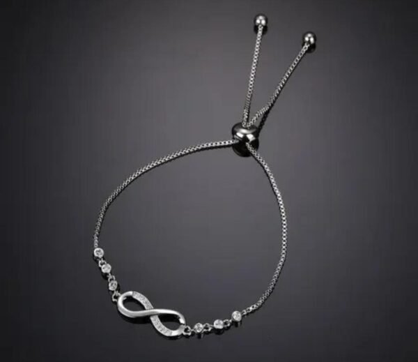 Silver-plated infinity bracelet displayed against a black background to emphasize the brilliance of the silver finish and intricate design.